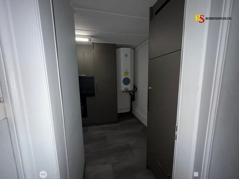 A narrow, dimly lit hallway with a tiled floor, white walls, and a water heater unit visible in the background.