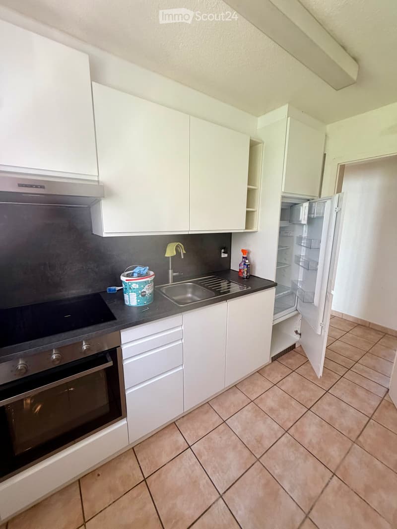 Modern kitchen with white cabinets, stainless steel appliances, and tiled flooring. Features an open refrigerator, sink, and countertop items.
