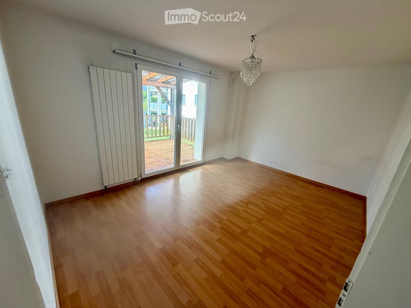 Empty room with wooden flooring, white walls, a sliding glass door leading to a wooden deck, and a chandelier hanging from the ceiling.