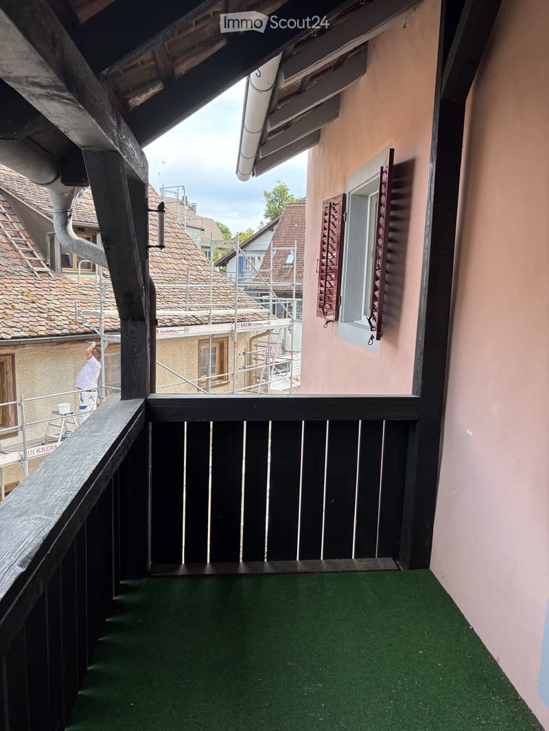 Balcony with green artificial turf flooring, wooden railing, and a view of neighboring buildings under construction.
