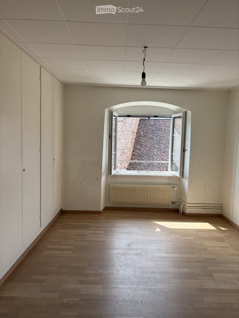 Empty room with wooden flooring, white walls, a large arched window, and a radiator below it.