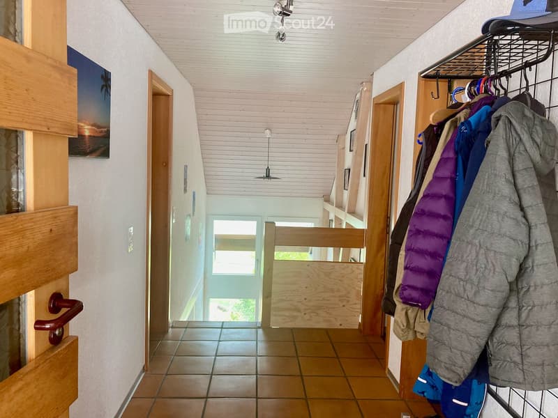 tiled floor, wooden doors, white walls, clothes hanging on rack, picture on wall, window at end of hallway