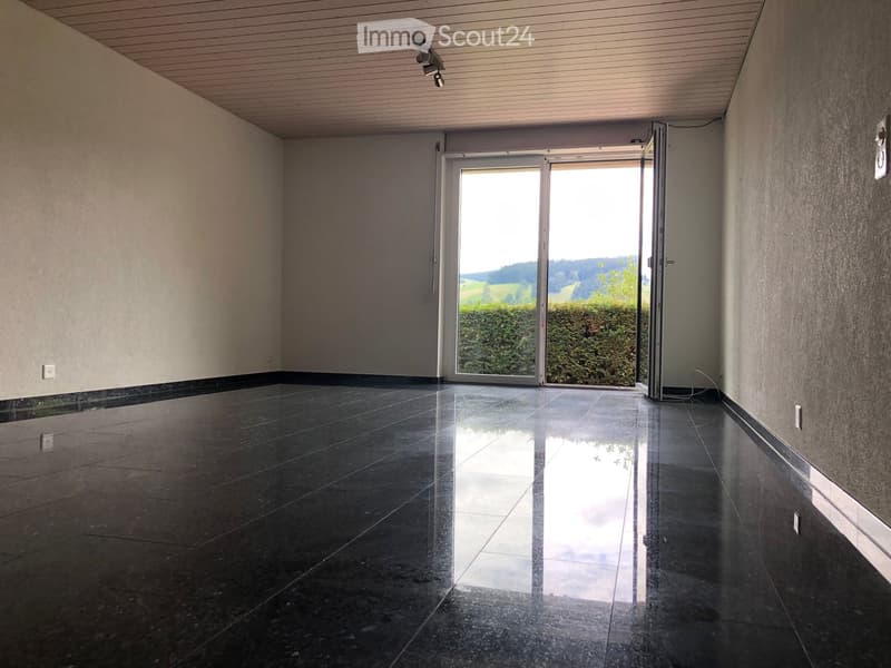 Empty hallway with polished dark tiled floor, light-colored walls, and a large glass sliding door leading to an outdoor view.