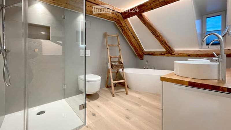 Modern bathroom with exposed wooden beams, a glass-enclosed shower, a toilet, a freestanding bathtub, a sink with a modern faucet, and a wooden ladder leaning against the wall.