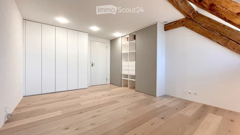 Empty room with light wooden flooring, white walls, built-in wardrobes, and exposed wooden beams on the ceiling.