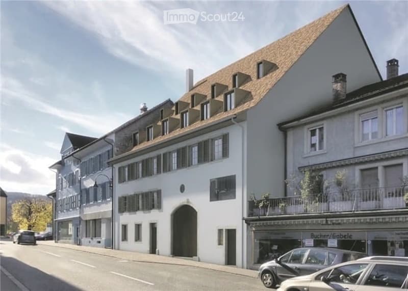 A multi-story residential building with a classic European architectural style, featuring a pitched roof, dormer windows, and white exterior walls.