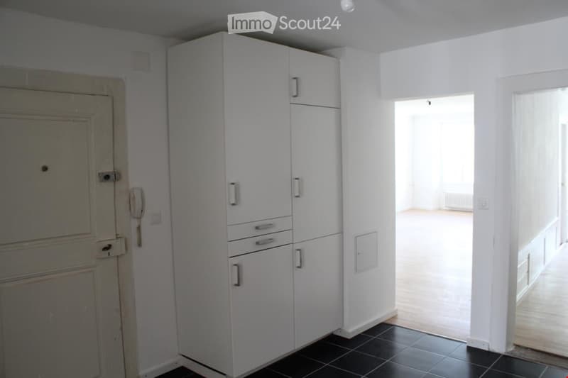 Empty room with white walls, black tiled floor, white built-in cabinetry, and an open doorway leading to another room.