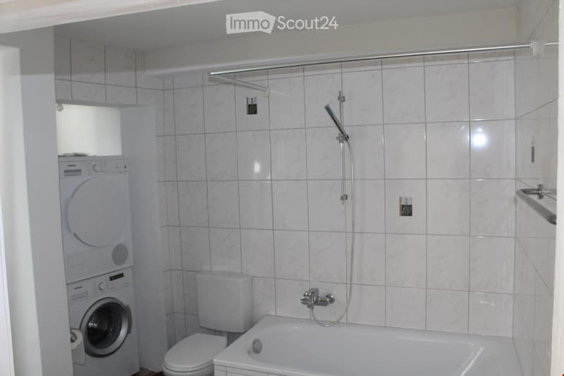 Modern bathroom with white tiled walls, a bathtub, toilet, shower, and a private washing machine.