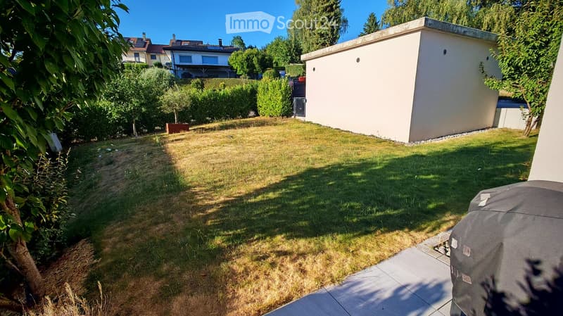 Well-maintained garden with a lawn, trees, and a small shed in the background.