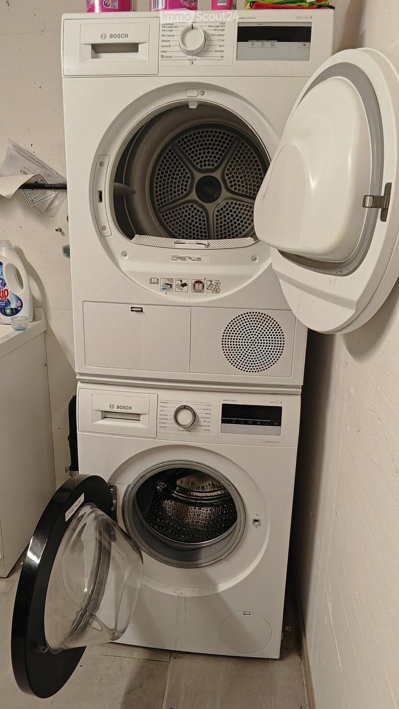 A Bosch washing machine and dryer are stacked vertically, with both doors open, showing the interior. A bottle of laundry detergent is visible on the left side.