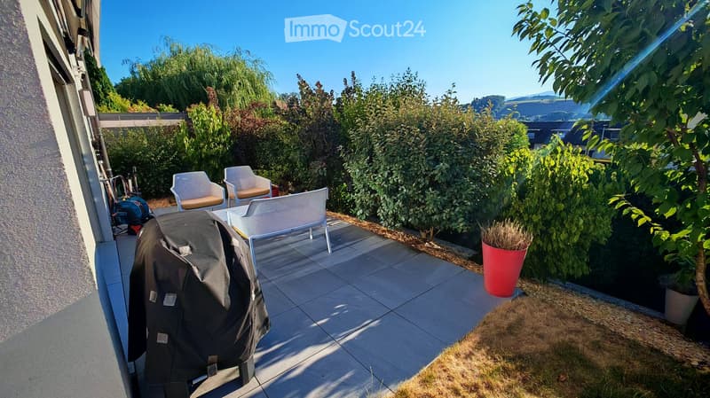 Balcony with tiled floor, two white chairs, a small table, and a covered grill.