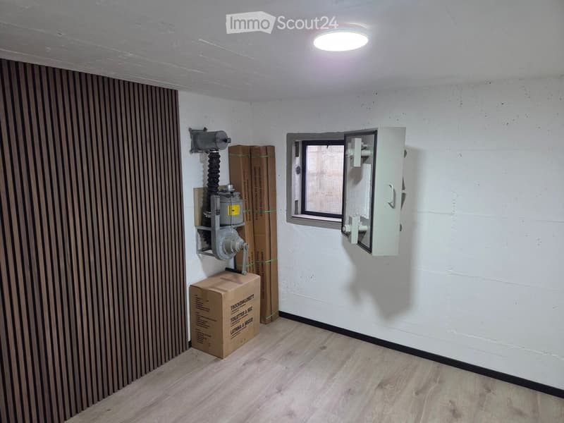Empty room with wooden flooring, white walls, a small window, and several cardboard boxes stacked against the wall.