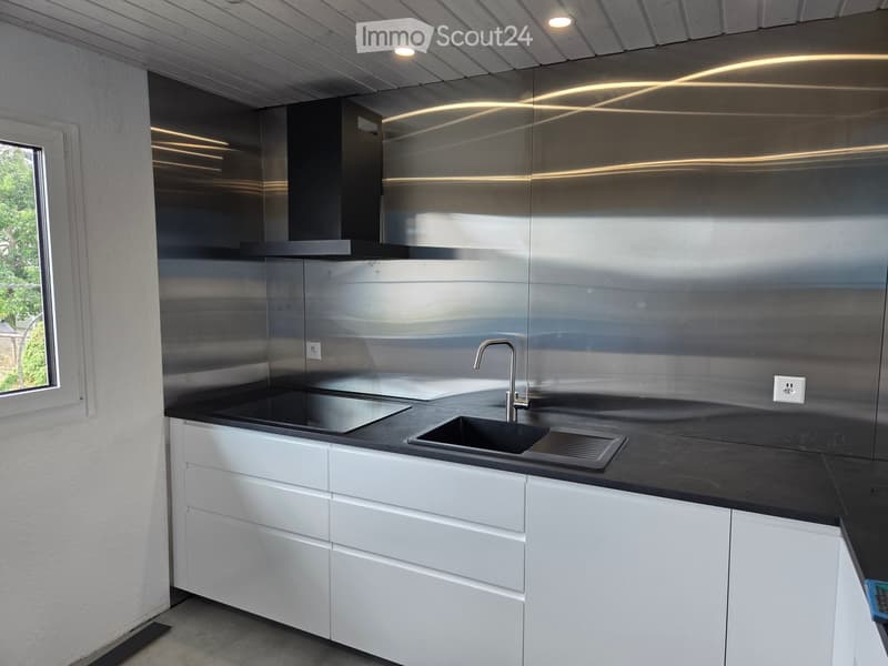 Modern kitchen with white cabinets, black countertops, stainless steel backsplash, and a sink with a modern faucet.