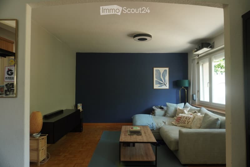 Modern living room with dark blue accent wall, light grey sectional sofa, wooden coffee table, side table, floor lamp, and decorative items.