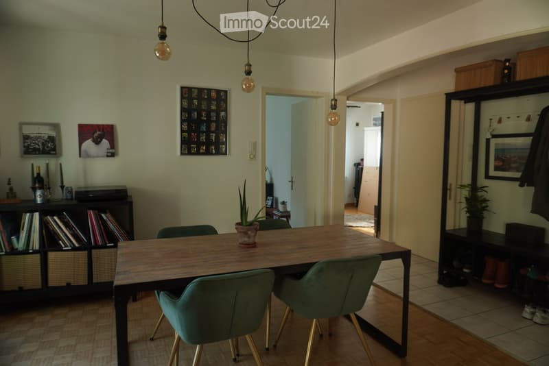 Dining area with a wooden table, green chairs, bookshelf, and decorative items.