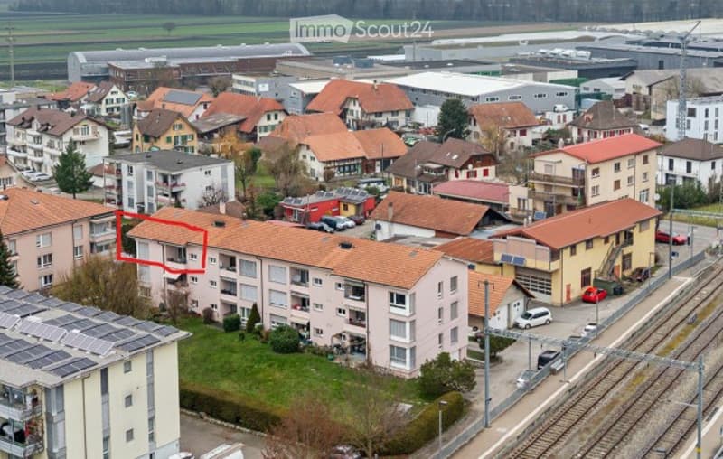 Aerial view of a residential area with multiple apartment buildings, red-tiled roofs, and surrounding greenery.