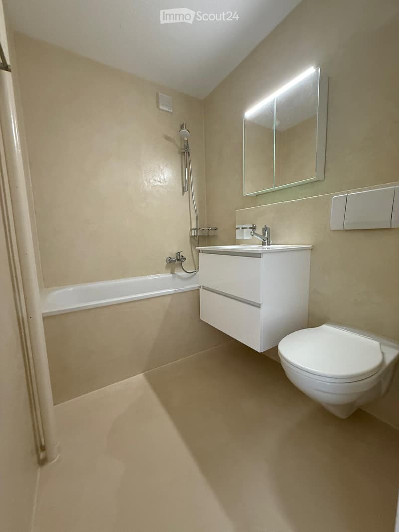 Modern bathroom with a bathtub, sink, toilet, and mirror. Light-colored tiles and sleek fixtures.