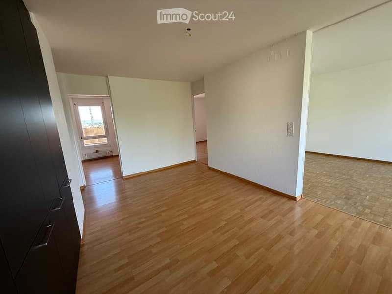 Empty hallway with wooden flooring, white walls, and a door leading to another room.