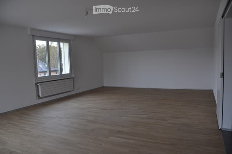 Empty room with wooden flooring, white walls, and a large window with a radiator below it. No furniture or equipment is present.