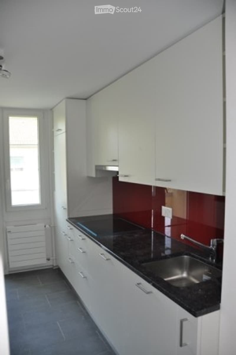 Modern kitchen with white cabinets, black countertop, stainless steel sink, and a window providing natural light.