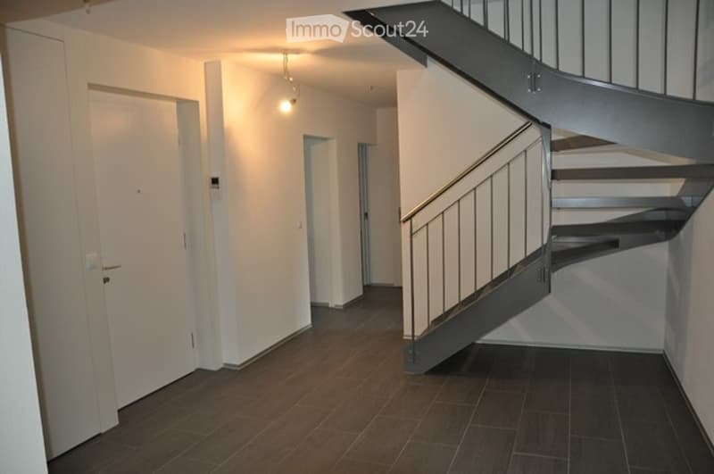 Empty hallway with wooden flooring, white walls, and a staircase leading upwards.
