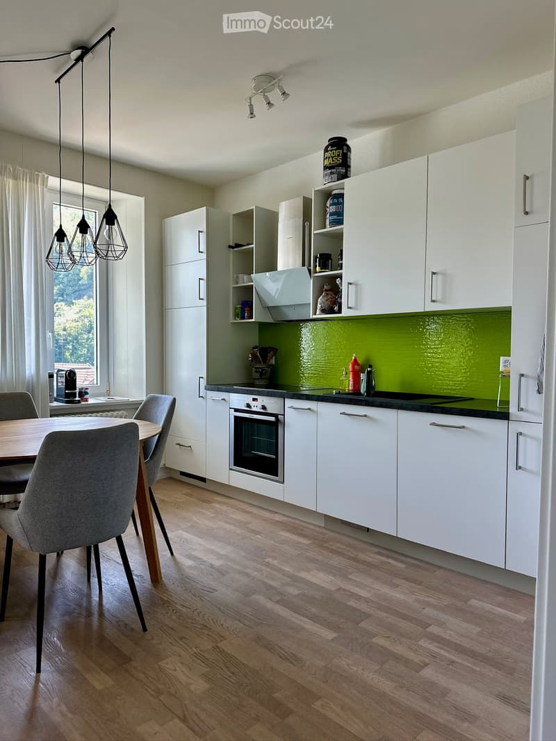 Modern kitchen with white cabinets, green backsplash, and wooden flooring. Includes a dining area with a table and chairs.