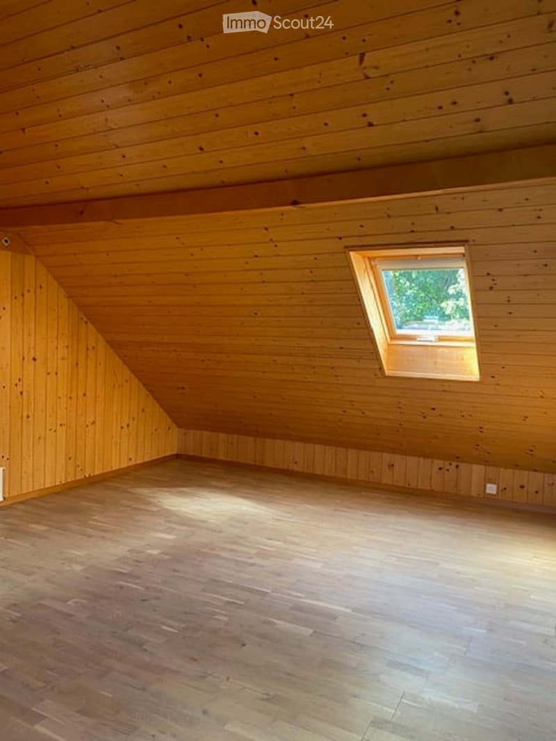 Empty attic room with wooden walls, ceiling, and floor, featuring a skylight window allowing natural light to enter.