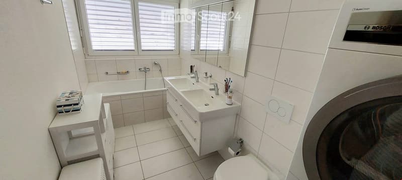 Bathroom. Modern bathroom with white tiles, a bathtub, double sink, mirror, and a toilet. Features include a towel rack, toothbrush holder, and a power outlet.