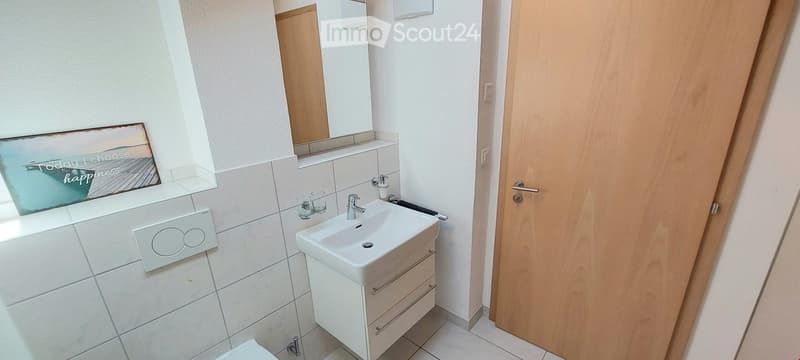 Bathroom. Modern bathroom with white tiles, a white sink with a cabinet, a mirror, and a picture frame on the wall.