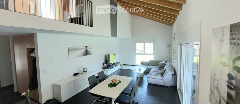 Furnished Room. Modern living and dining area with white walls, dark flooring, and wooden ceiling beams. Features a white sectional sofa, coffee table, dining table with chairs, TV on a stand, and a cabinet.