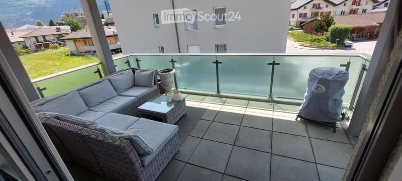 Balcony / Terrace. Balcony with a view of the surrounding area, featuring a grey wicker sofa, a small table, and a covered grill.