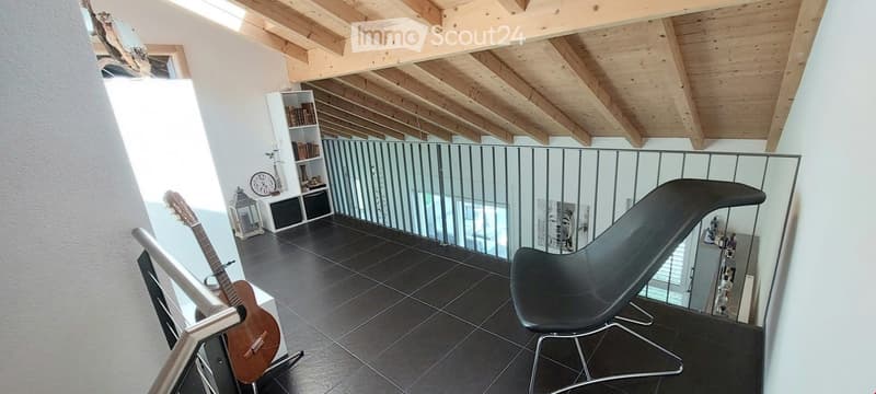 Furnished Room. Balcony with dark tiled floor, wooden slatted ceiling, modern black chair, guitar, bookshelf, and clock.