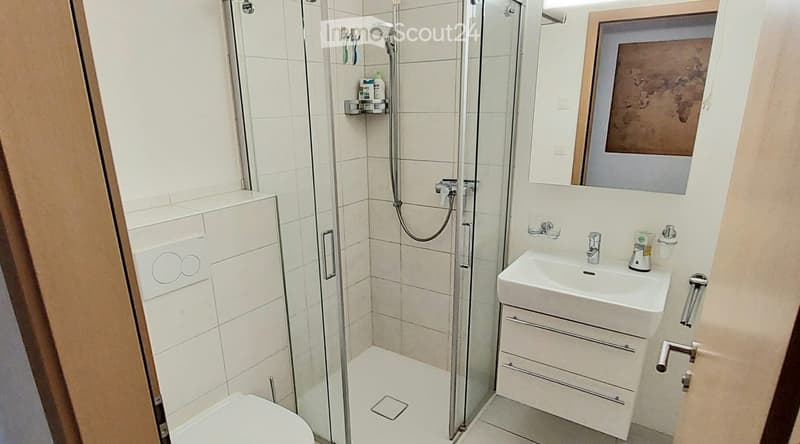 Bathroom. Modern bathroom with a white tiled shower stall, a white toilet, a white sink with a mirror above it, and a small shelf holding toiletries.