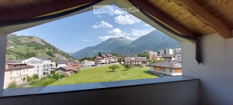 Balcony / Terrace. Balcony with wooden ceiling and railing, overlooking a town with houses, green fields, and mountains in the background.