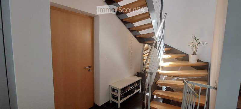 Corridor / Hallway. A modern hallway with a wooden staircase, a small shoe rack, and a potted plant on the landing.