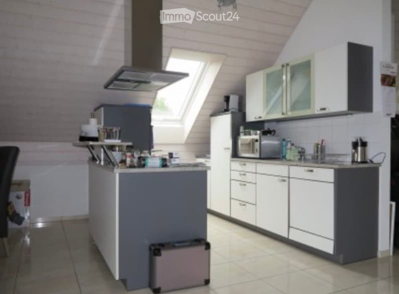 Modern kitchen with white cabinets, a central island, and various appliances including a microwave, oven, and refrigerator. The space features a skylight window and a sleek, contemporary design.