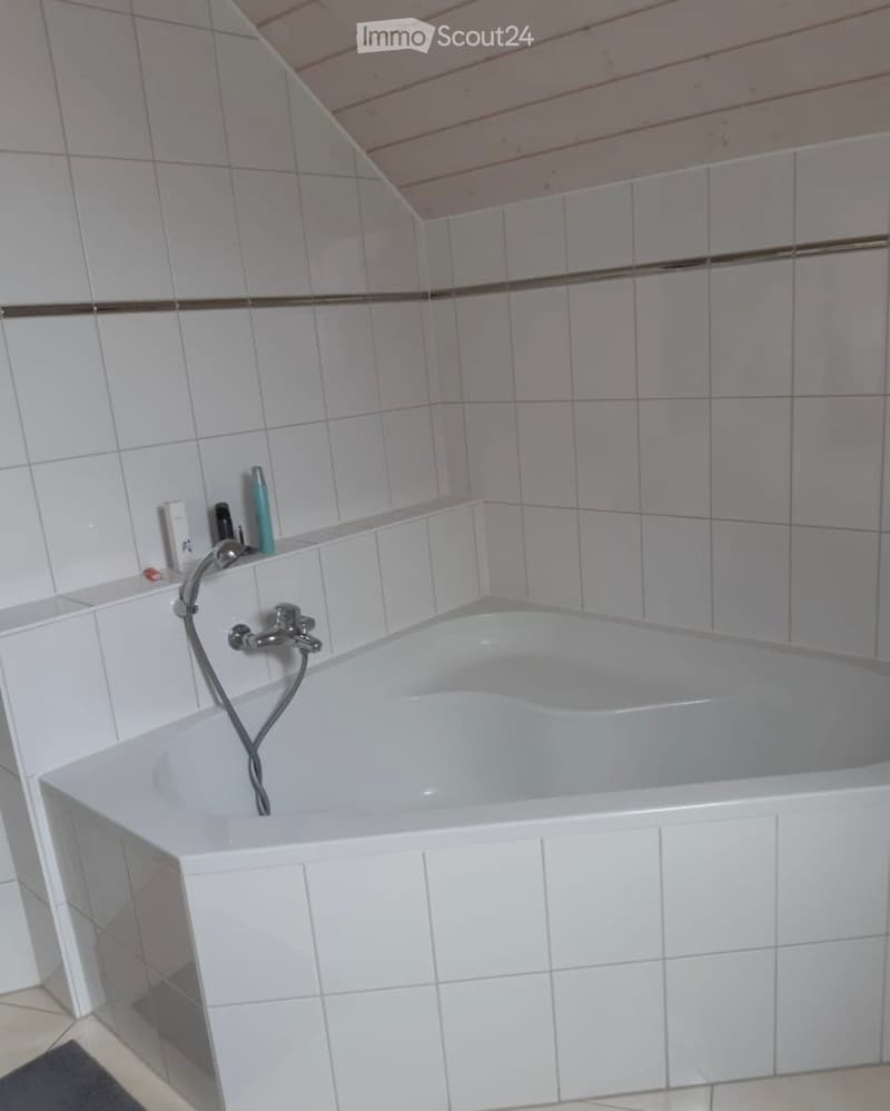 Bathtub with a handheld shower hose and faucet, surrounded by white tiled walls and a wooden ceiling.