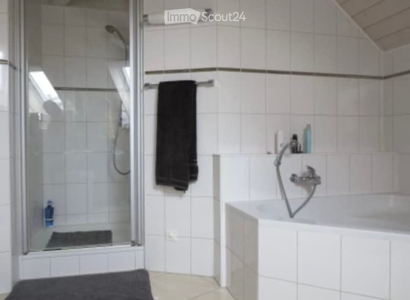 Modern bathroom with white tiled walls and floor, featuring a bathtub, shower stall, towel rack, and various toiletries.