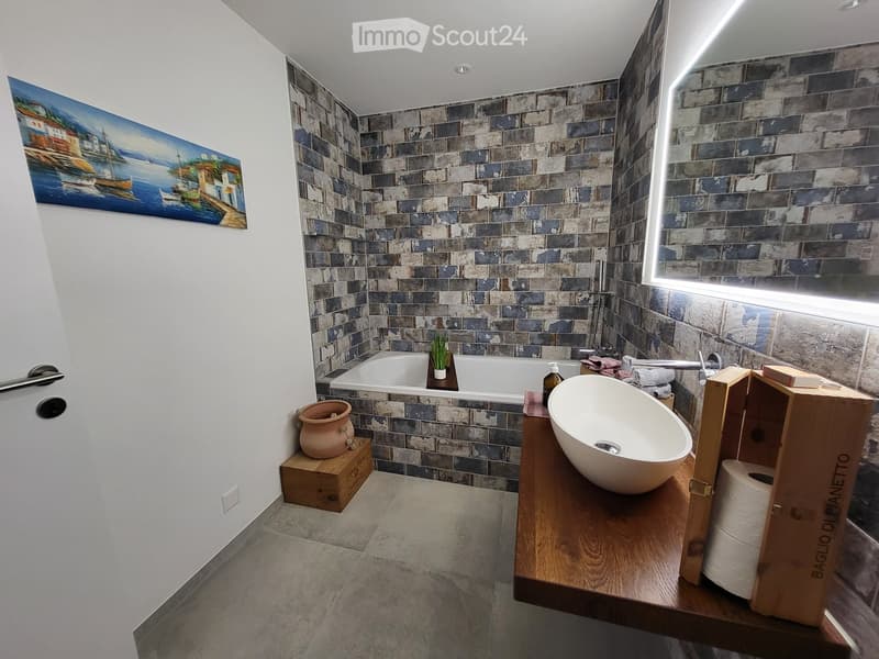 Bathroom: white sink, bathtub, wooden countertop, blue brick wall, mirror, decorative painting, wooden box for toilet paper