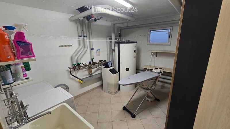 Utility room with a washing machine, ironing board, shelves holding cleaning supplies, water heater, control panel, and a sink.