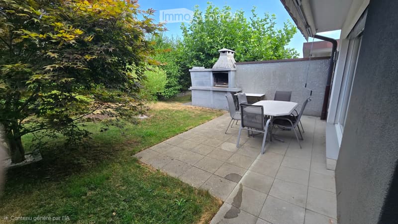 Outdoor patio area with a dining table and chairs, a barbecue, and a small grassy lawn surrounded by trees.