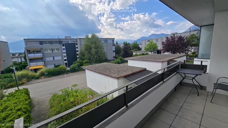 Balcony with tiled floor, metal railing, small table and chair, overlooking a residential area with buildings and greenery.