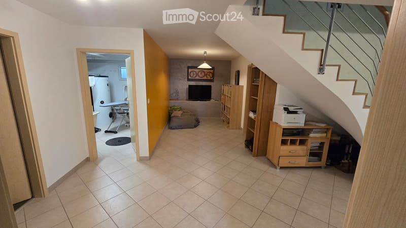 A furnished room with a tiled floor, a staircase, a screen, a table, a chair, shelves, a printer, and a stool.