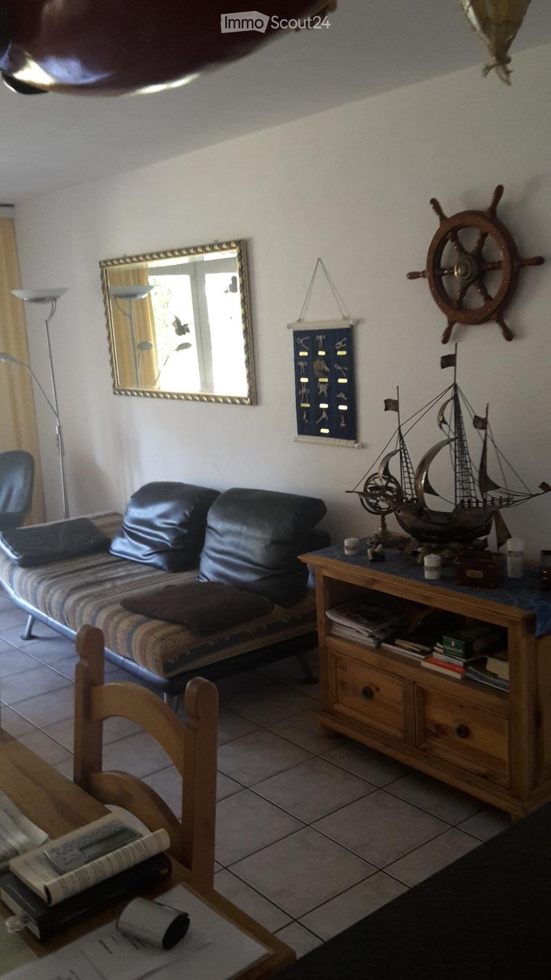 A cozy living room with a sofa, a wooden table, a chair, a mirror, a model ship, and a floor lamp.