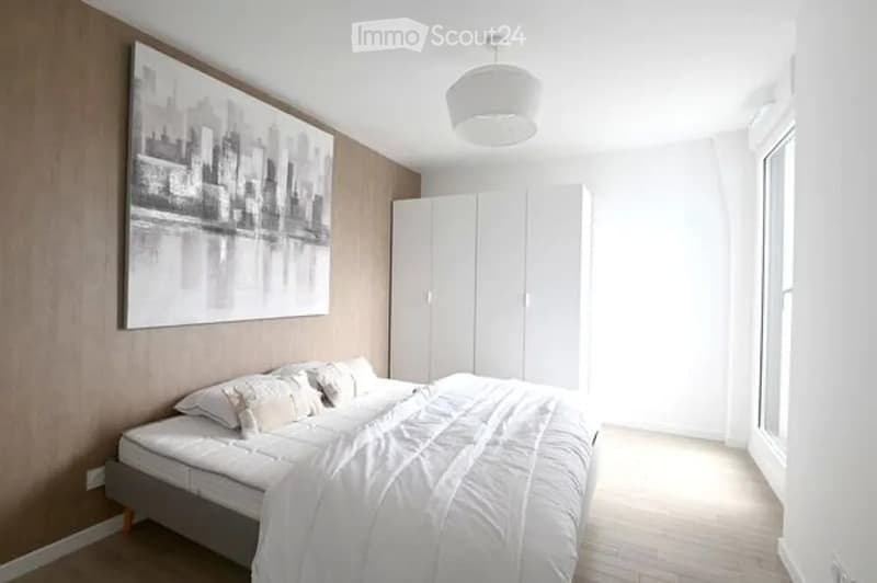 Modern bedroom with a white bed, pillows, and a blanket, a large white wardrobe, and a large black and white cityscape picture on the wall.