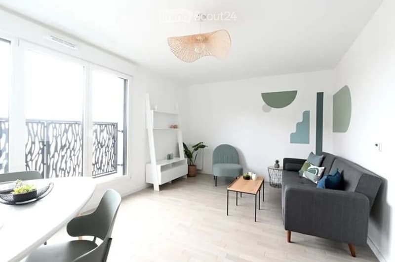 Modern living room with large windows and balcony access, featuring a grey sofa, coffee table, armchair, shelf, and dining area with a table and chairs.