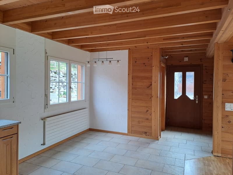 Bright hallway with exposed wooden beams, white plaster walls, large windows, and a wooden door leading to another room.