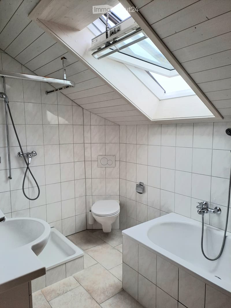 Modern bathroom with white tiles, a bathtub, toilet, sink, and a shower. Features skylight windows and a sleek design.