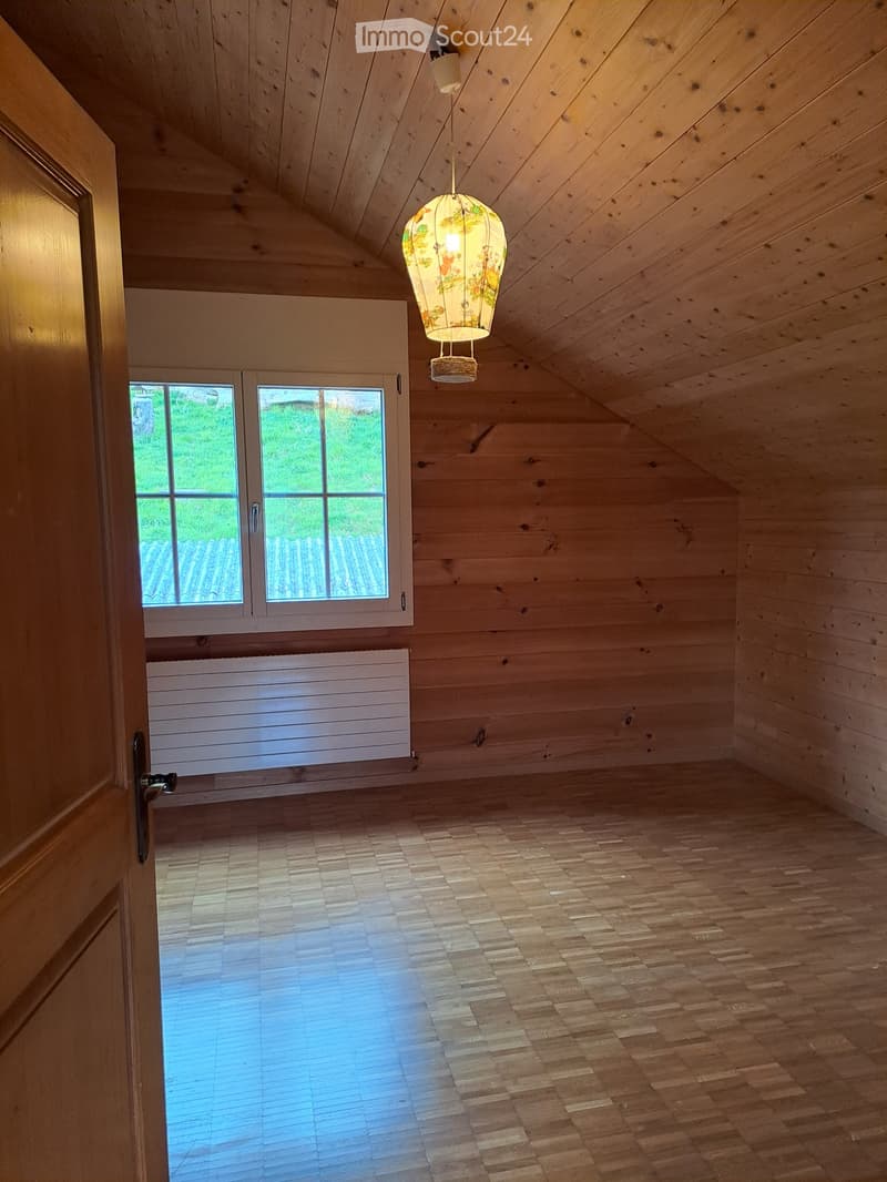 Empty attic room with wooden walls, ceiling, and floor, large windows, and a decorative hanging lantern light fixture.