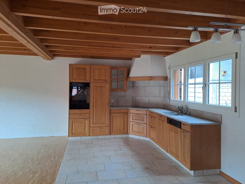 Bright, airy kitchen with wooden cabinets, granite countertops, and a modern stainless steel sink. The space features exposed wooden beams on the ceiling and large windows allowing natural light to fill the room.